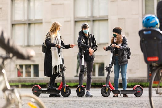 Trendy fashinable group of friends riding public rental electric scooters in urban city environment at fall. New eco-friendly modern public city transport in Ljubljana, Slovenia.