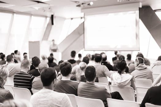 Man giving presentation in lecture hall. Male speeker having talk at public event. Participants listening to lecture. Rear view, focus on people in audience.