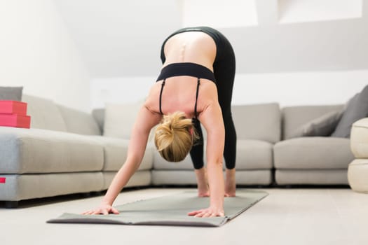 Beautiful blonde woman doing home workout indoors. Woman practice yoga at home. Fit girl using workout tutorials for healthy active lifestyle. Woman using quarantine for home workouts. Stretching