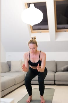 Beautiful blonde woman doing home workout indoors. Woman practice yoga at home. Fit girl using workout tutorials for healthy active lifestyle. Woman using quarantine for home workouts. Stretching