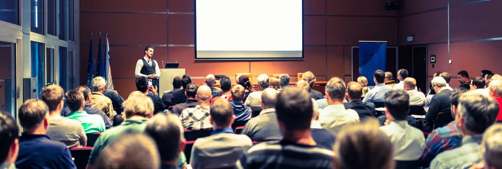 Speaker giving a talk in conference hall at business meeting event. Rear view of unrecognizable people in audience at the conference hall. Business and entrepreneurship concept.