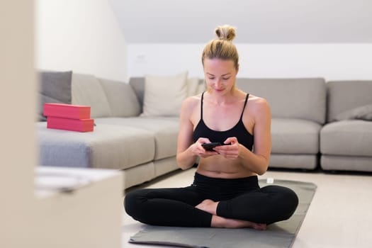 Beautiful blonde woman doing home workout indoors. Woman practice yoga at home. Fit girl using workout tutorials for healthy active lifestyle. Woman using quarantine for home workouts. Stretching