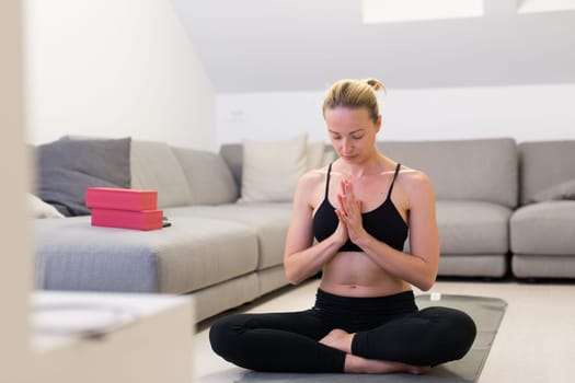 Beautiful blonde woman doing home workout indoors. Woman practice yoga at home. Fit girl using workout tutorials for healthy active lifestyle. Woman using quarantine for home workouts. Stretching