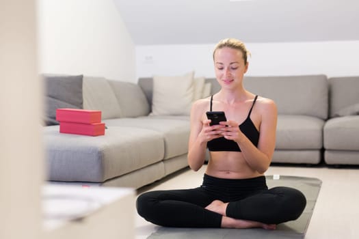 Beautiful blonde woman doing home workout indoors. Woman practice yoga at home. Fit girl using workout tutorials for healthy active lifestyle. Woman using quarantine for home workouts. Stretching