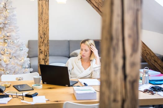 Young businesswoman wearing cosy warm bathrobe working remotly from home in winter Christmas time during 2020 corona virus pandemic. Work from home, selter in place, concept.