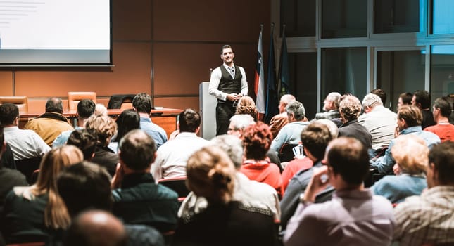 Speaker giving a talk in conference hall at business meeting event. Rear view of unrecognizable people in audience at the conference hall. Business and entrepreneurship concept.