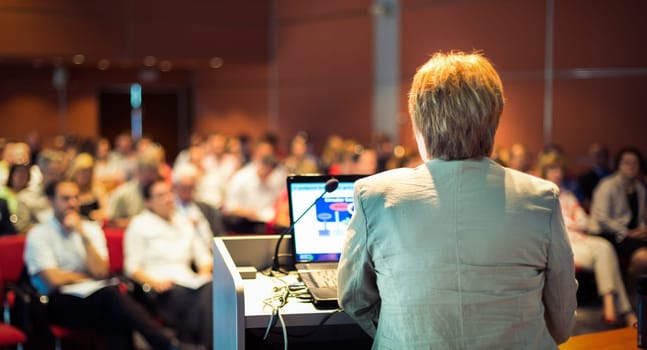 Senior business woman lecturing at Conference. Audience at the lecture hall.