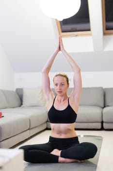 Beautiful blonde woman doing home workout indoors. Woman practice yoga at home. Fit girl using workout tutorials for healthy active lifestyle. Woman using quarantine for home workouts. Stretching