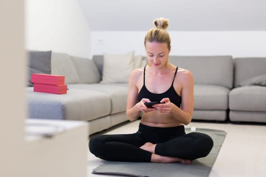 Beautiful blonde woman doing home workout indoors. Woman practice yoga at home. Fit girl using workout tutorials for healthy active lifestyle. Woman using quarantine for home workouts. Stretching