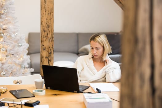 Young businesswoman wearing cosy warm bathrobe working remotly from home in winter Christmas time during 2020 corona virus pandemic. Work from home, selter in place, concept.