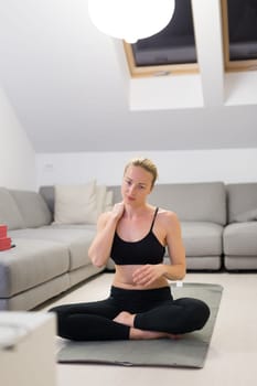 Beautiful blonde woman doing home workout indoors. Woman practice yoga at home. Fit girl using workout tutorials for healthy active lifestyle. Woman using quarantine for home workouts. Stretching
