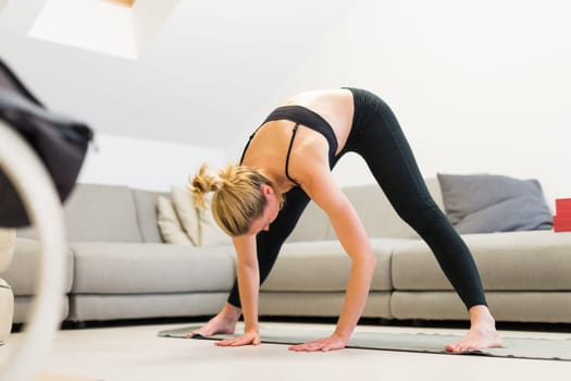 Beautiful blonde woman doing home workout indoors. Woman practice yoga at home. Fit girl using workout tutorials for healthy active lifestyle. Woman using quarantine for home workouts. Stretching