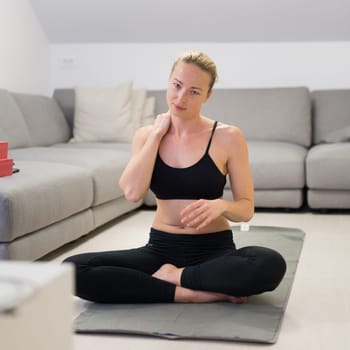 Beautiful blonde woman doing home workout indoors. Woman practice yoga at home. Fit girl using workout tutorials for healthy active lifestyle. Woman using quarantine for home workouts. Stretching