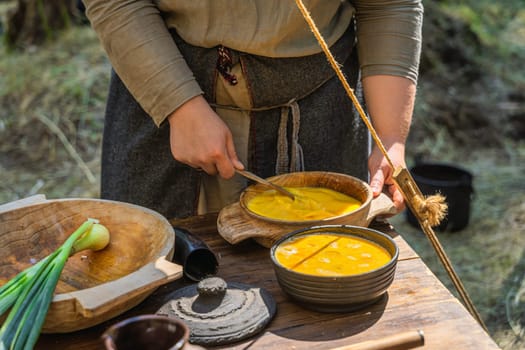 Scrambled egg in wooden bowls prepared by a woman in traditional clothing. Homemade food on the table at historical reenactment of Slavic or Vikings lifestyle from around 11th century, Cedynia, Poland