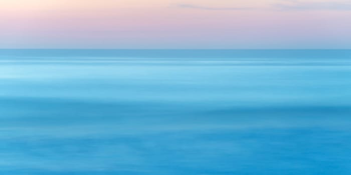 Long exposure of seascape at sunset, blue sea water abstract background, pastel pink sky