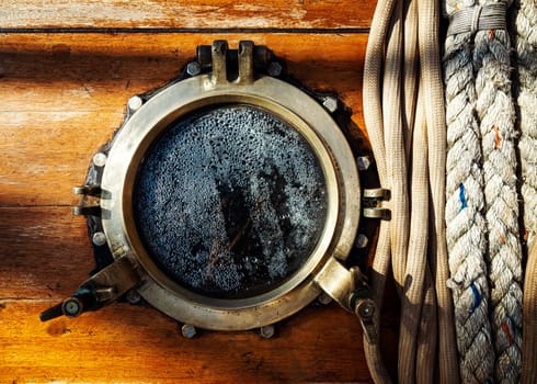 Vintage sailboat brass porthole and ropes on wooden wall. Mist on the glass window.