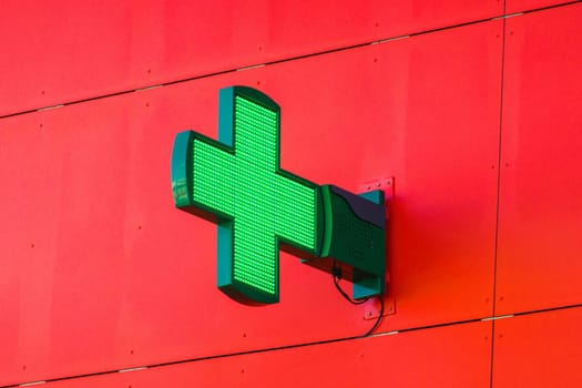 Green pharmacy LED light sign on metal red wall, in France