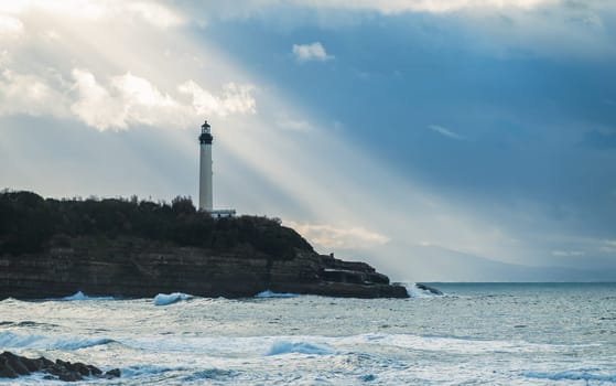 Biarritz lighthouse with sun rays in France, Atlantic Ocean in the foreground