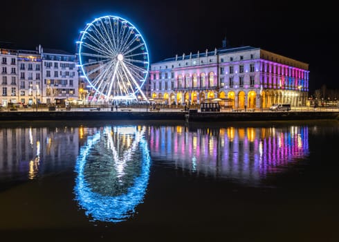 The ferris wheel and the town hall at night in Bayonne, France. Reflection on the river.
