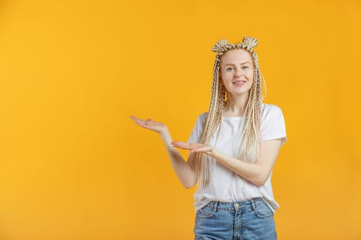 Smiling blonde caucasian woman in casual is pointing to empty space, isolated in yellow background.