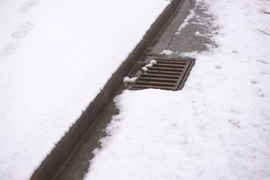 2 - Road covered in heavy snow with only the curbside drain showing. As the snow melts, the local area is at risk of flooding from all the water.