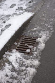 7 - Urban highway drain covered in thawing snow fall. Water runs along the curbside and into the surface storm drain. This area is at risk of flooding