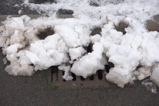 11 - Close up of a kerbside storm drain nearly blocked by snow. Urban water management problem as the melting snow can cause flooding.