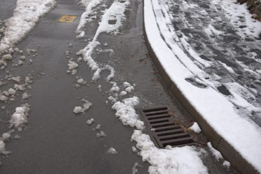 9 - Road and pavement covered in thawing snow. Road is partially cleared by cars, but sledge tracks and footsteps still line the pavement.