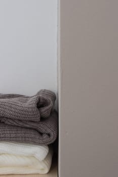 A stack of wool sweaters on the shelf. Grey and white sweater. Warm and cozy. Knitted clothing.