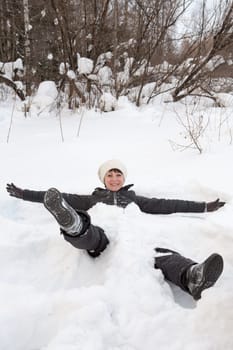 Side view of a beautiful young woman laying down on a frozen snow lake moving her arms up and down creating an angel figure shape, playing games while on vacation during a sunny winter day