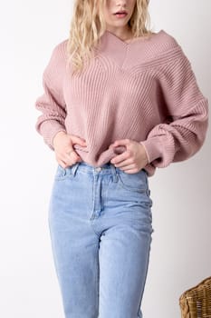 Photo of a teenage woman posing in high-waisted blue jeans and a sweater. Details of women's clothing