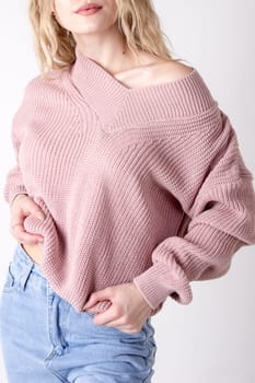 Photo of a teenage woman posing in high-waisted blue jeans and a sweater. Details of women's clothing