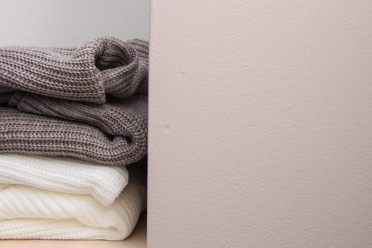 A stack of wool sweaters on the shelf. Grey and white sweater. Warm and cozy. Knitted clothing.