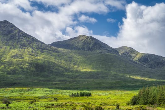 Green fields, trees and mountains illuminated by sunlight in Cronins Yard on trail to highest mountain in Ireland Carrauntoohil, Ring of Kerry Ireland
