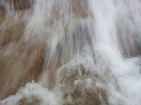 Blurred or unfocused view of flowing water stream in between stones. Flowing water background for texture and advertisements