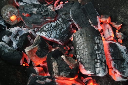 Fire on logs in fire pot with embers and burning coal. Bonfire with blazing red and orange fire flames. Fire background with woods and planks on fire at night view.