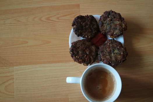 Delicious spicy fried round kebab served in white ceramic plate on a wooden floor with cup of hot tea.