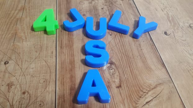 Plastic colored alphabets making words 4 july USA are placed on a wooden floor. These plastic letters can be used for teaching kids.
