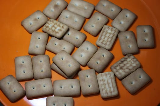Close up top view of of biscuit cookies. Many rectangular biscuits with small pores in red plate