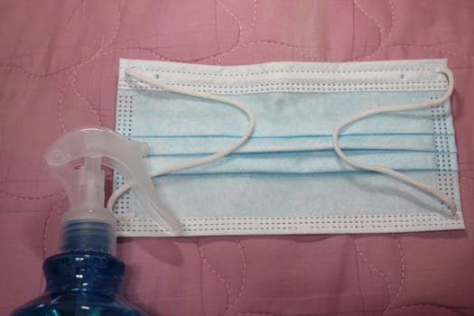 blue color cloth face mask with hand sanitizer bottle isolated on pink background
