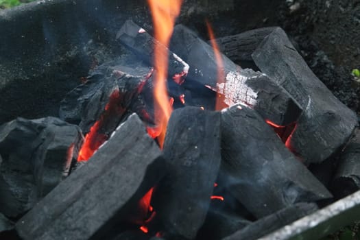 Fire on logs in fire pot with embers and burning coal. Bonfire with blazing red and orange fire flames. Fire background with woods and planks on fire at night view.