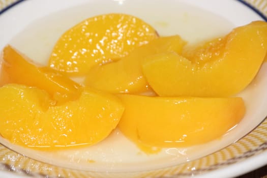 Closeup high angle view with selective focus of yellow peaches slices. Canned peaches halves sprinkled with syrup in white plate.