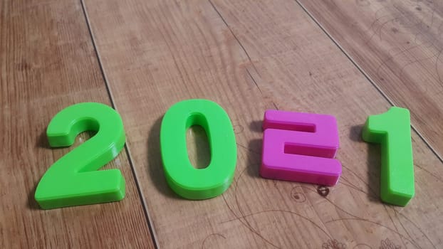 Plastic colored alphabets making words 2021 are placed on a wooden floor. These plastic letters can be used for teaching kids.