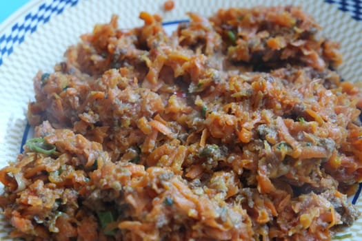 Top closeup view of a homemade dish made from carrot and vegetables served in a ceramic plate.