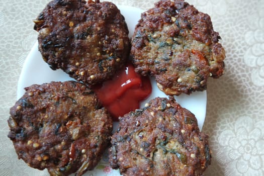 Delicious spicy fried round kebab served in white ceramic plate on a wooden floor with red sauce.