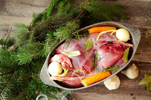 Roasted wild rabbit haunch with stewed vegetables in pan garnished with fresh herbs, flat lay