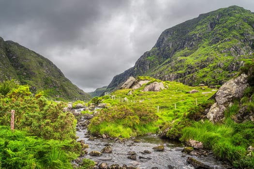 Small stream in beautiful green mountain valley, Gap of Dunloe, going between steep hills in Black Valley, County Kerry, Ireland