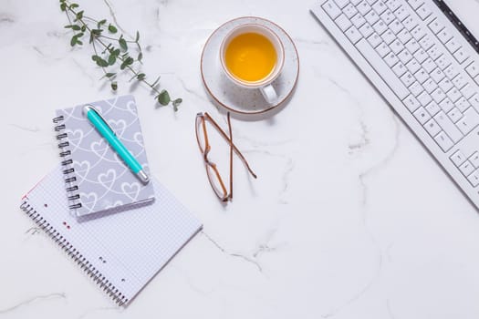 Flat lay home business desk with communication device with cup of tea and writing tools. Feminine business mockup, copyspace, white background.