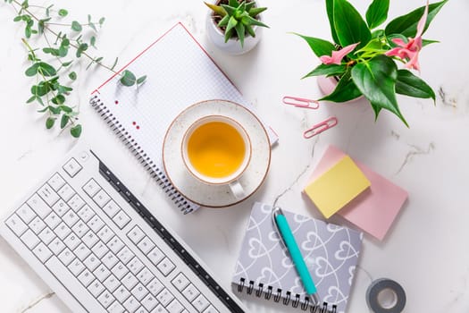 Flat lay home business desk with communication device with cup of tea and writing tools. Feminine business mockup, copyspace, white background.