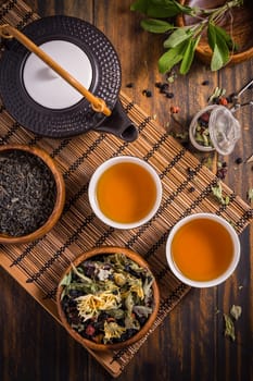 Herbal and fruit tea concept with teapot and infuser and assorted herbal leaves on wooden background